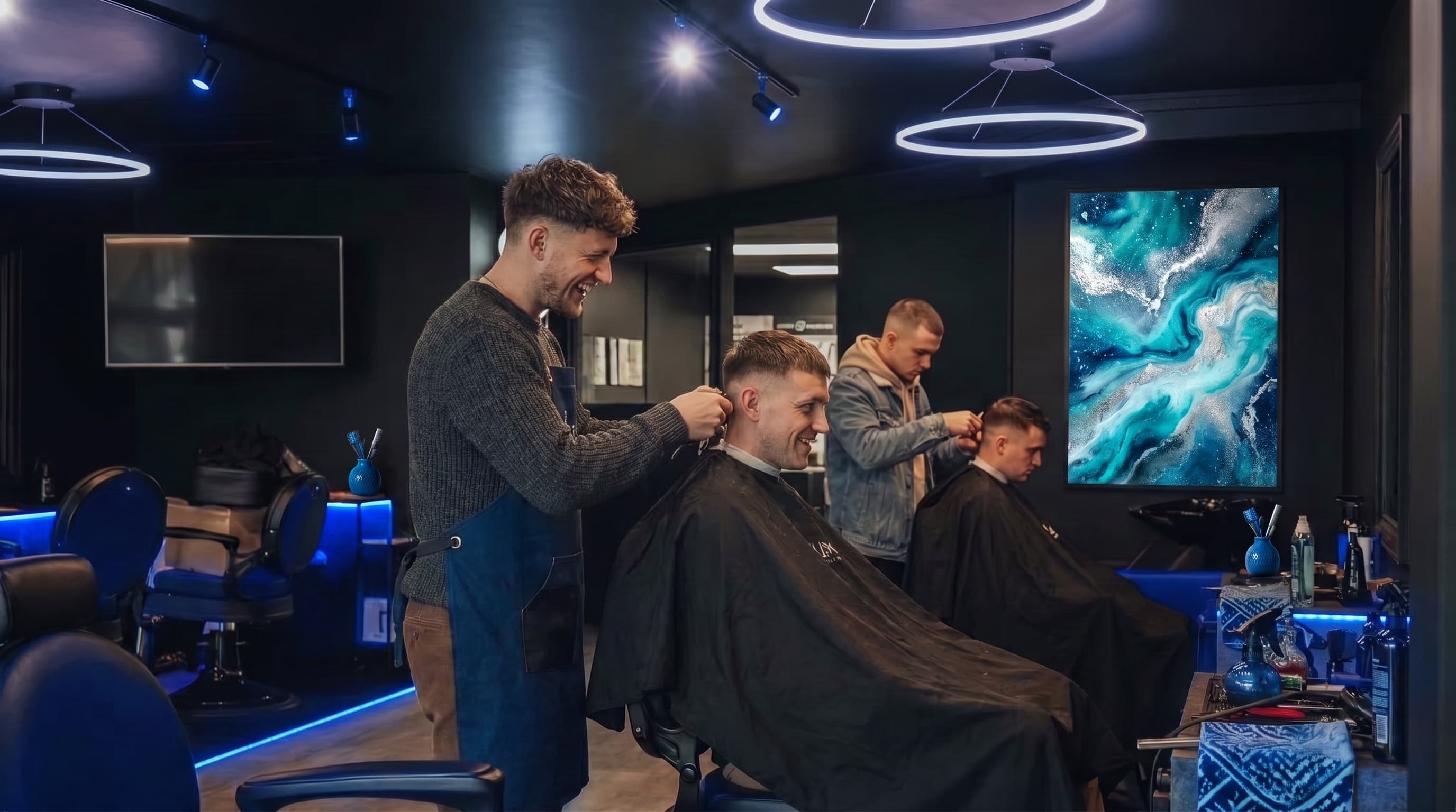 A modern barbershop with blue accent lighting and branded wall art, barbers giving fresh cuts